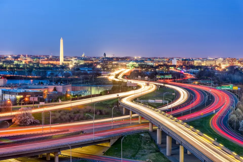 Fast-moving traffic lights on freeways in Washington, D.C. with Washington Monument in background at dusk.